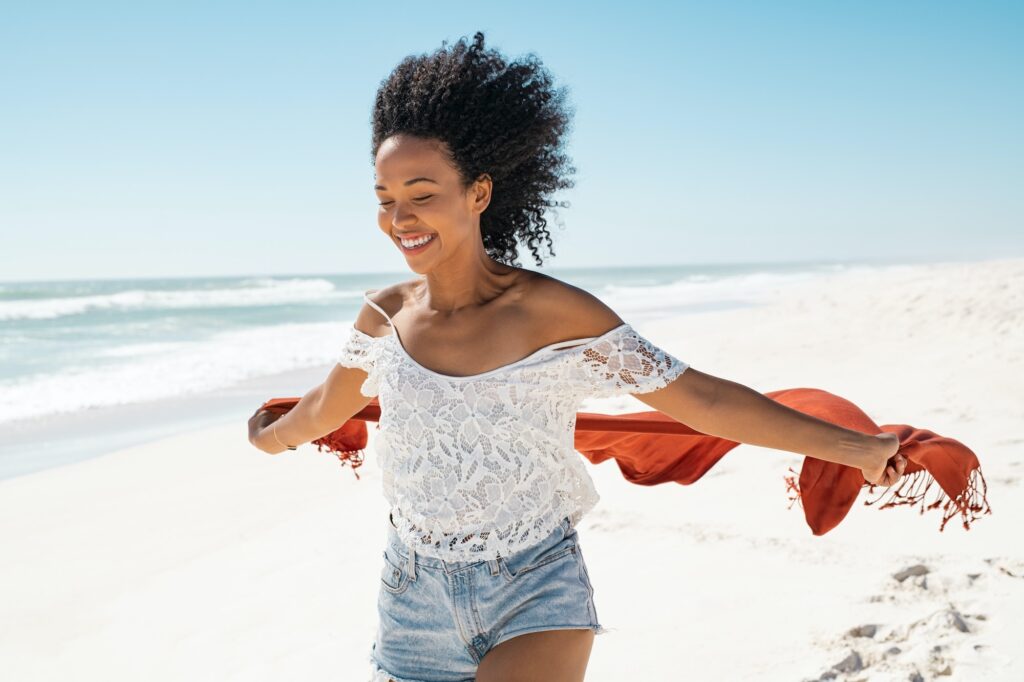 Carefree black woman running on beach with scarf