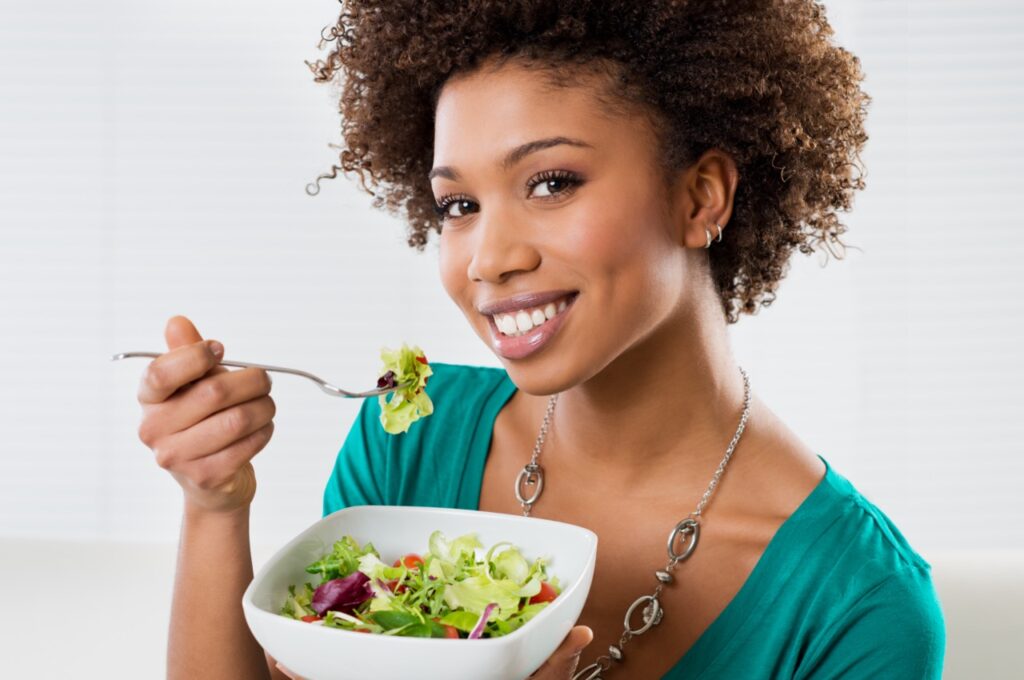 African-American woman eating a salad. Consuming a nutritious and balanced diet is an important step to cancer prevention.