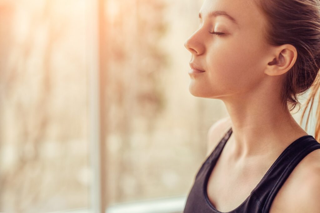 Young woman doing breathing exercise while practicing mindfulness.
