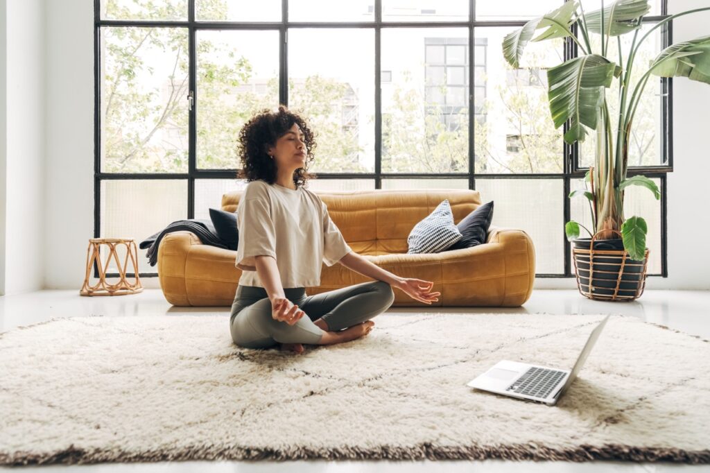 Woman meditating at home practicing mindfulness to reduce stress and anxiety.