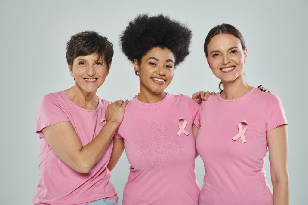 Breast cancer awareness, interracial women smiling on grey backdrop, different generations.