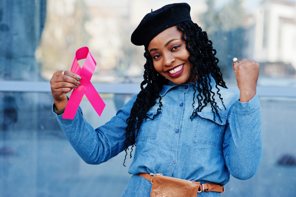 African american women in jeans wearing a black beret holding pink ribbon for breast cancer awareness.