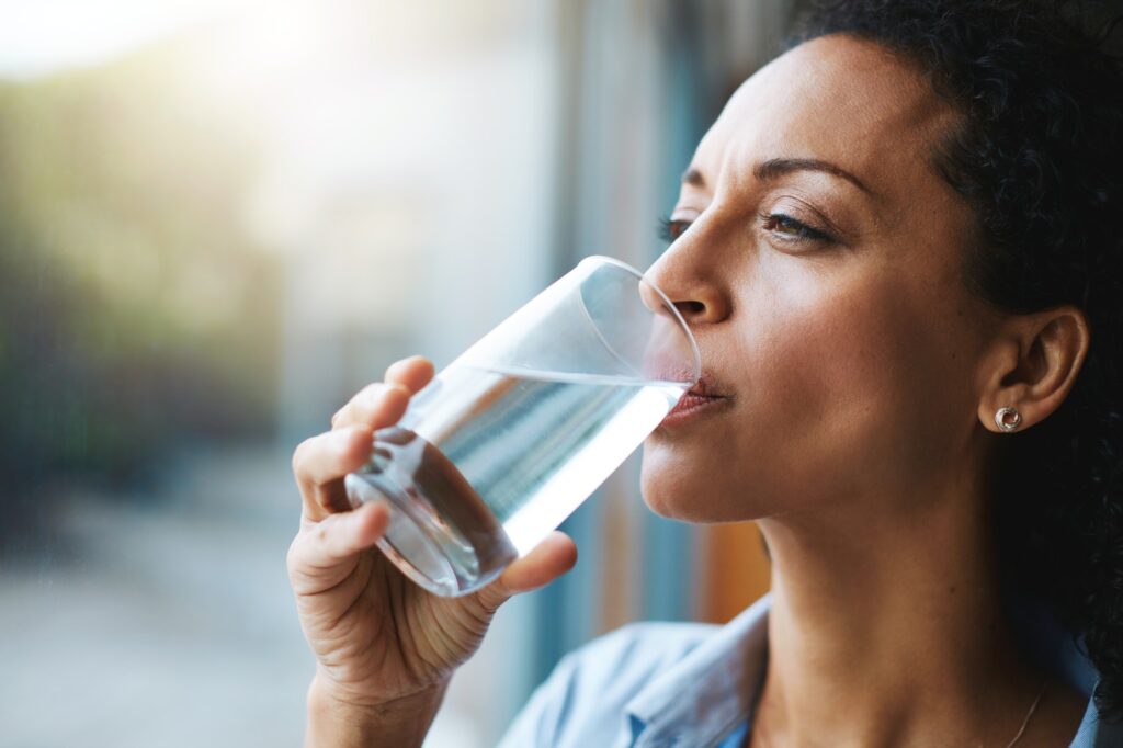 Woman drinking a glass of water hydrating at home.