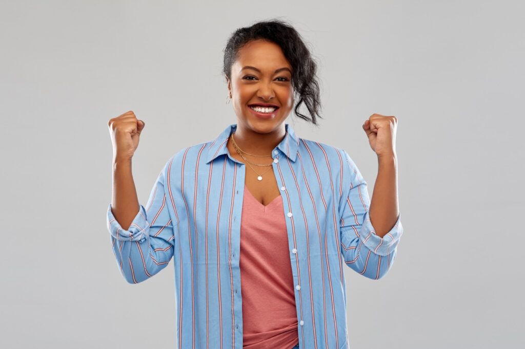 Happy young African American woman celebrating victory over grey background.