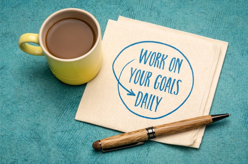 work on your goals daily - motivational reminder, handwriting on a napkin with a cup of coffee.